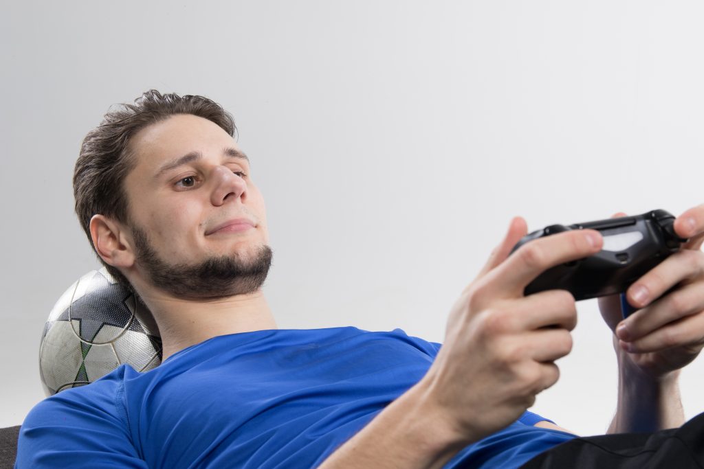 Young man usingh soccer ball for a pillow plays video games.