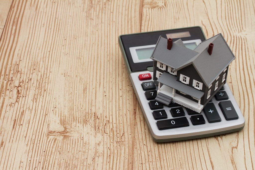 A gray house and calculator on wood background with copy space for your message